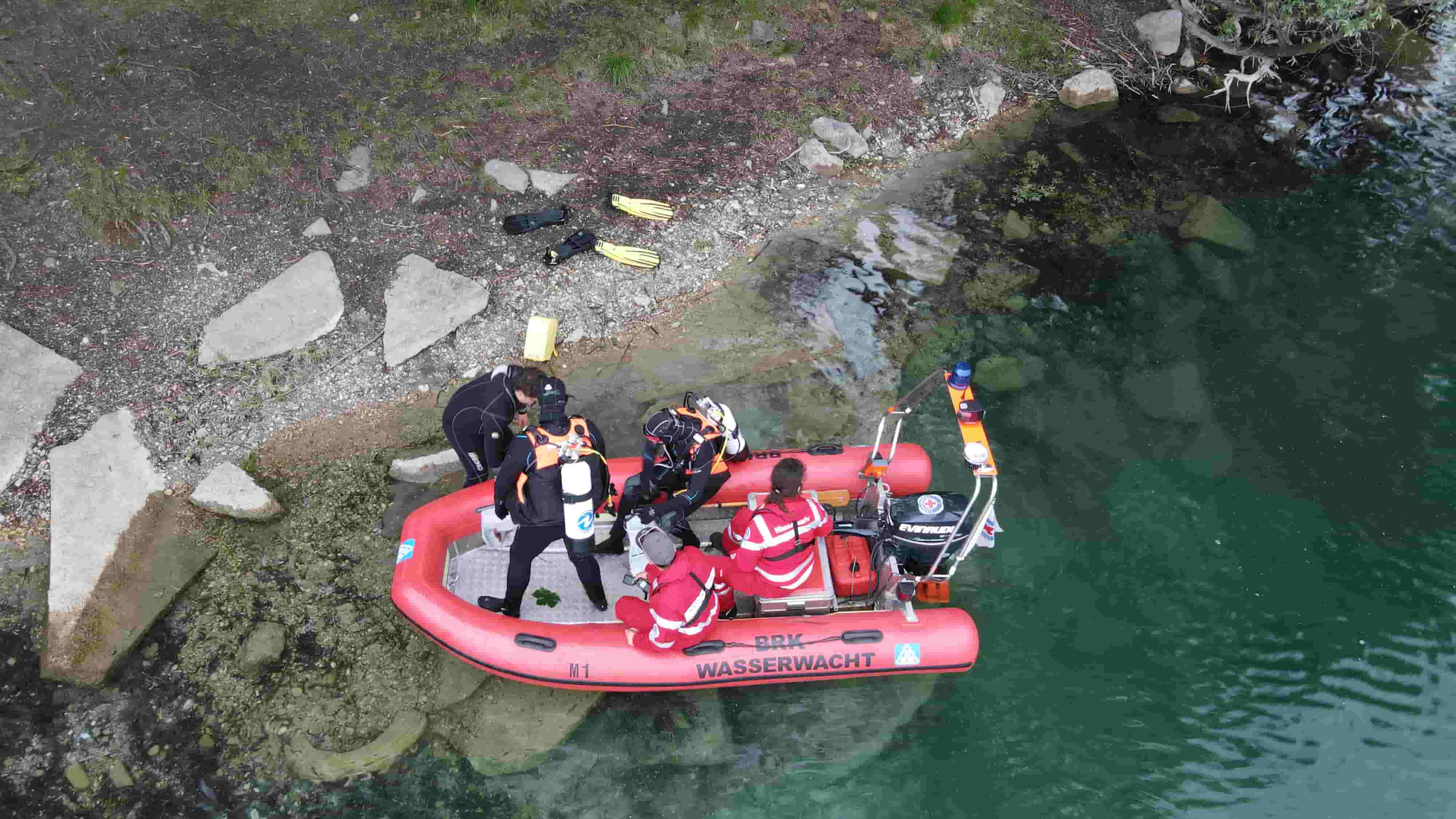 Drei Taucher steigen von einem Rettungsboot der Wasserwacht mit einem Bootsführer.