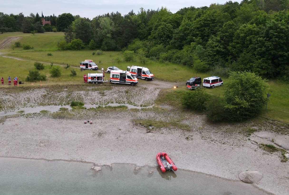 Bei einer Übung der Wasserwacht stehen vor einem See stehen fünf Einsatzfahrzeuge, im Boot liegt ein Rettungsboot.